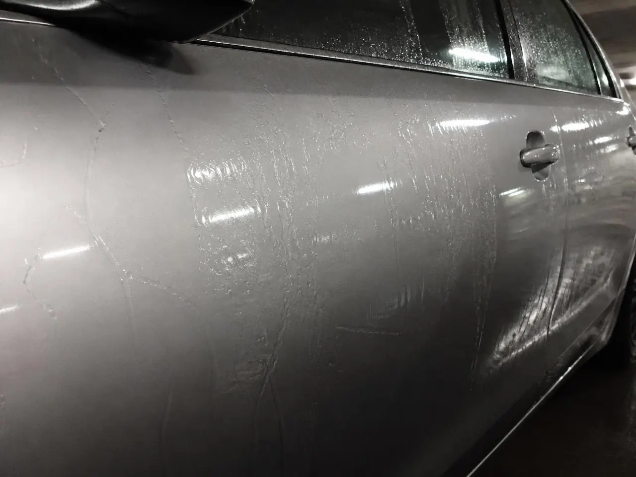 Wet grey car door before ceramic coating: water spreads in flat sheets across the paint