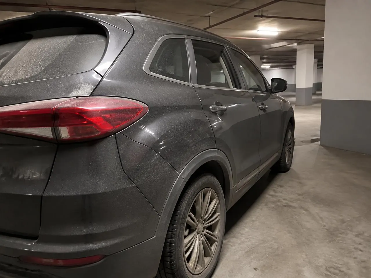 Rear quarter panel and wheel of a grey SUV before washing, covered in road film and brake dust