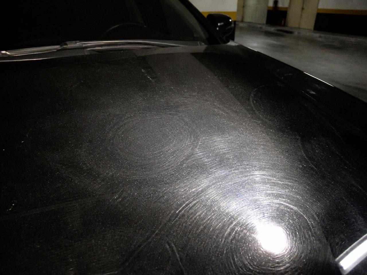 Black hood before polishing showing swirl marks and micro-scratches under an inspection light