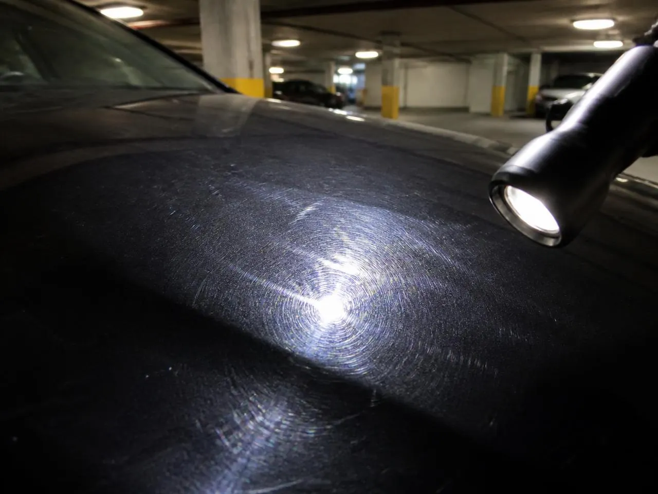 Black hood before polishing showing swirl marks and micro-scratches under an inspection light